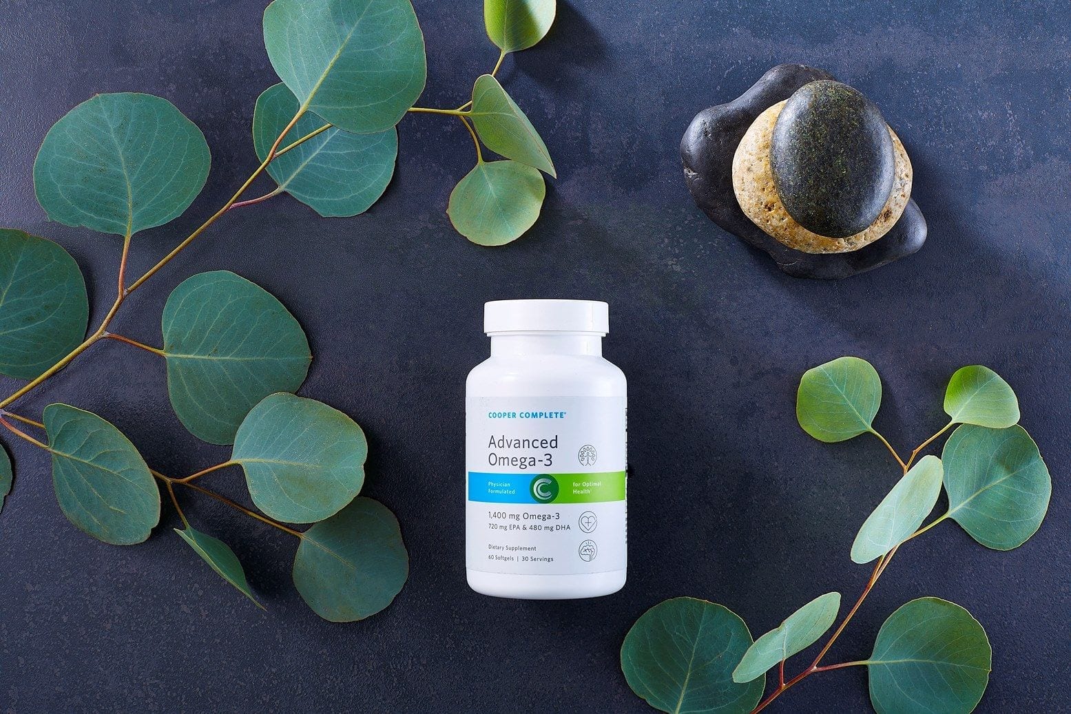Cooper Complete Advanced Omega 3 supplement Bottle on a dark slate surface with green branches and several small stacked rocks