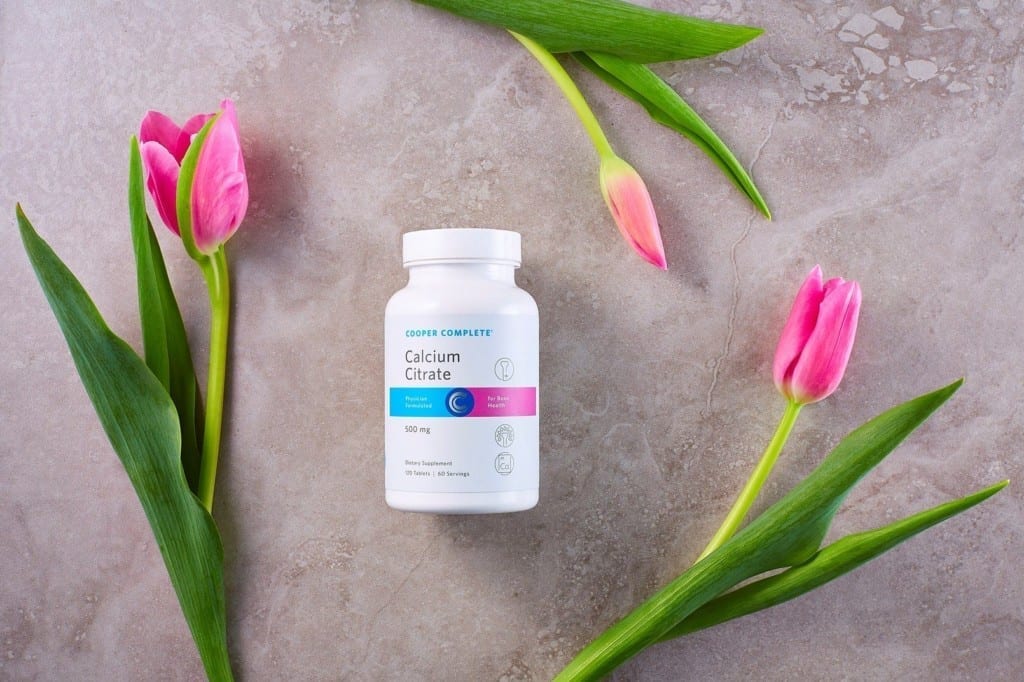 Cooper Complete Calcium Citrate Dietary Supplement bottle on a slate surface with several pink tulips