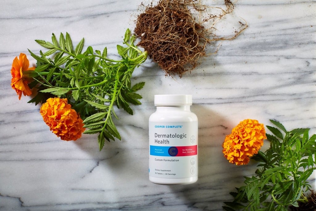 Cooper Complete Dermatologic Health dietary supplement bottle on a marble surface with marigold plants