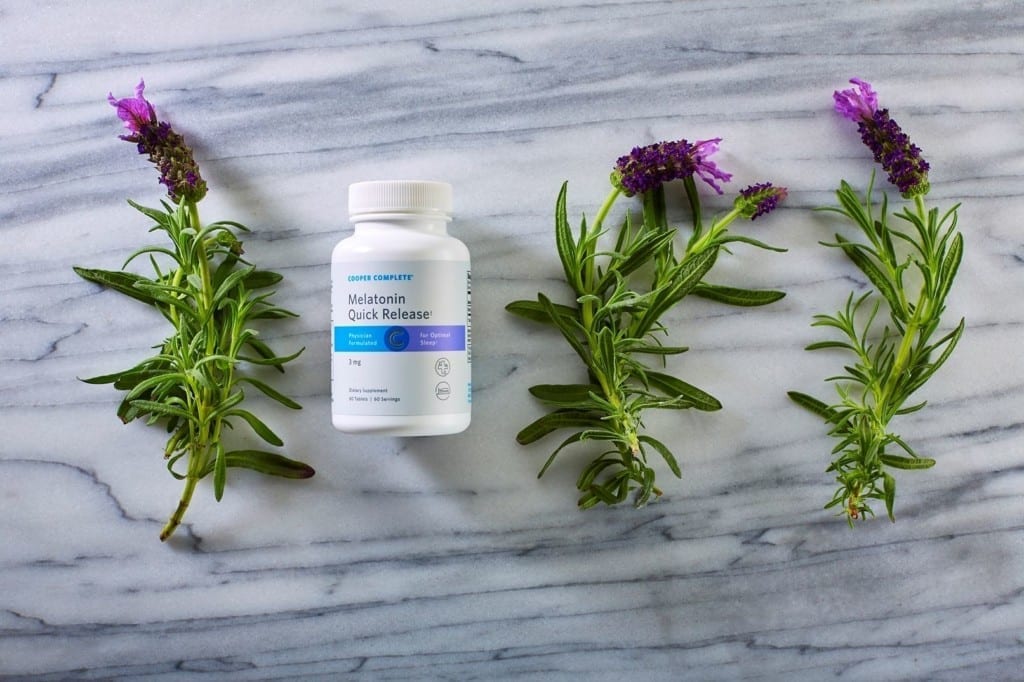 Cooper Complete Melatonin Quick Release dietary supplement bottle with purple flowers on a marble surface