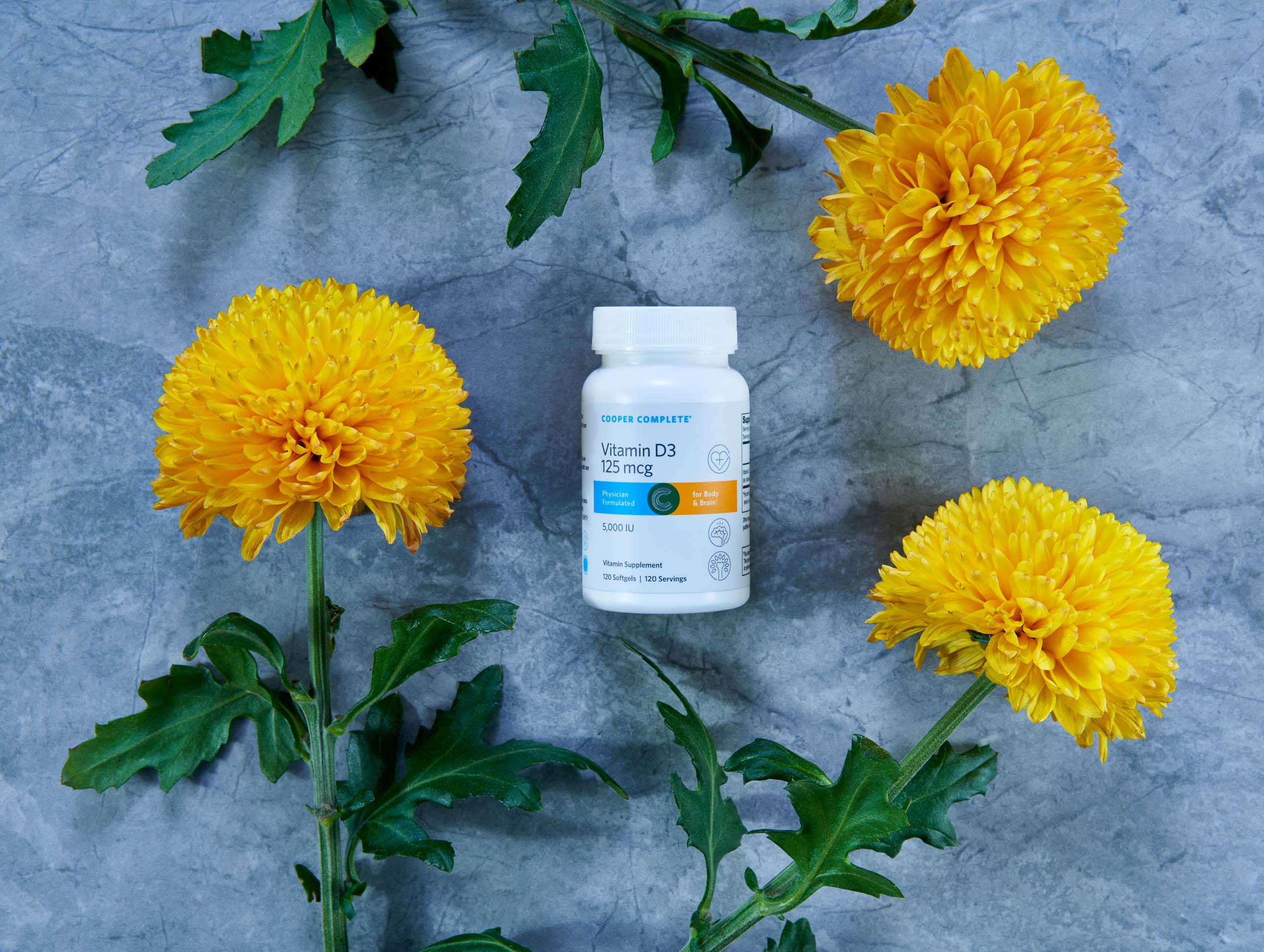 Photograph of Cooper Complete Vitamin D 3 125 mcg (5000 IU) Supplement bottle surrounded by merigolds