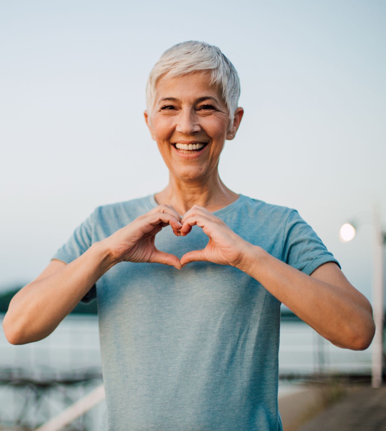 Photo of a smiling mature woman making the heart sign with her hands.