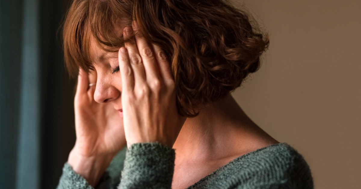Photo of a middle-aged woman hands on temples like her head hurts.