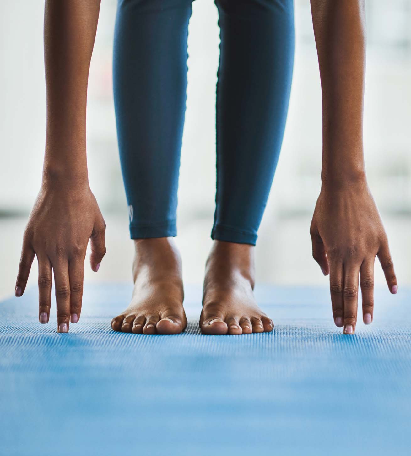 Photo of a young woman's arms and legs as her fingers touch the floor beside her toes in a deep stretch.