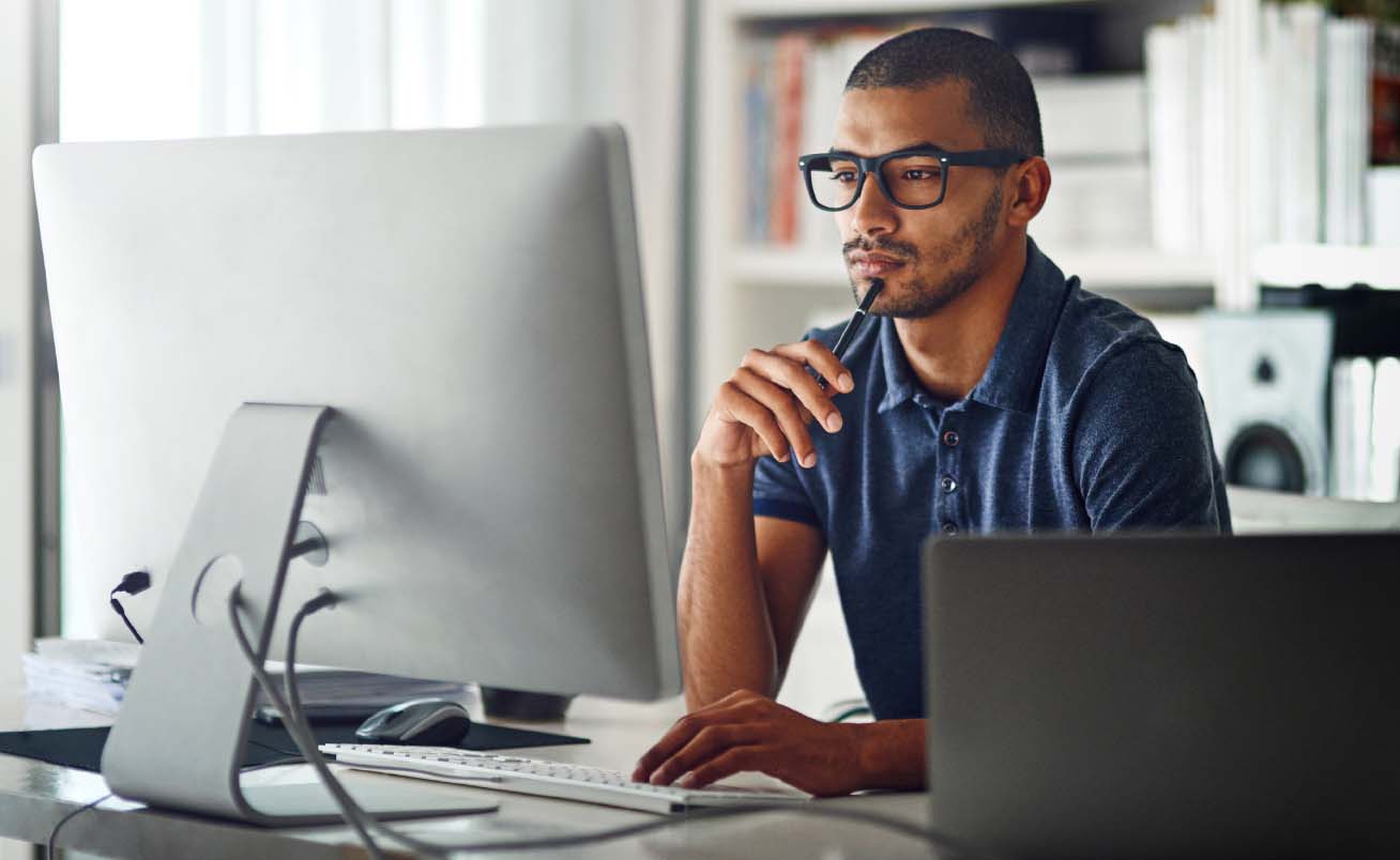 Photo of a young man deep in thought as he stares at the data on his computer monitor.