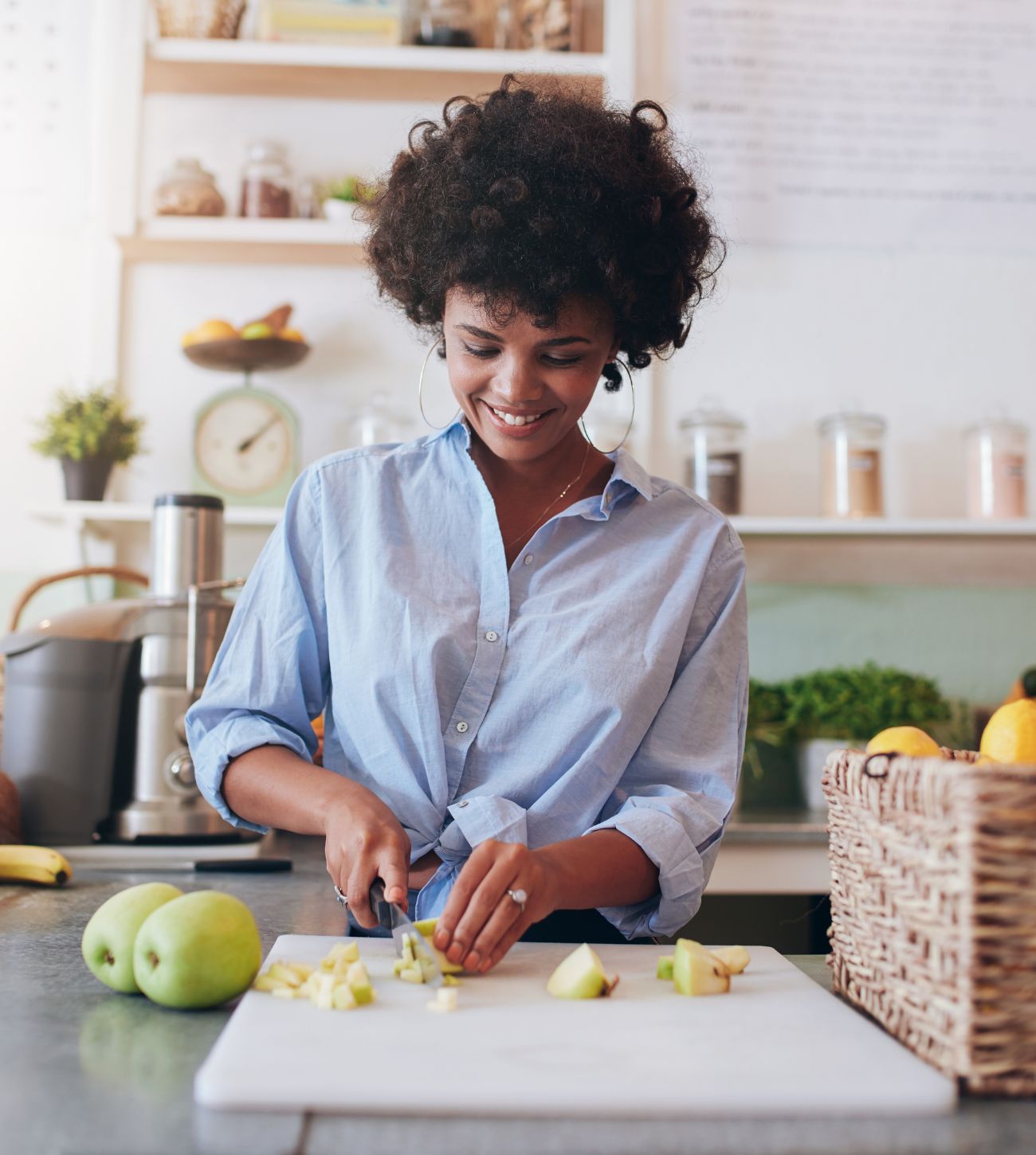 Photo of a young woman cutting green apples on a cutting board in the kitchen.
