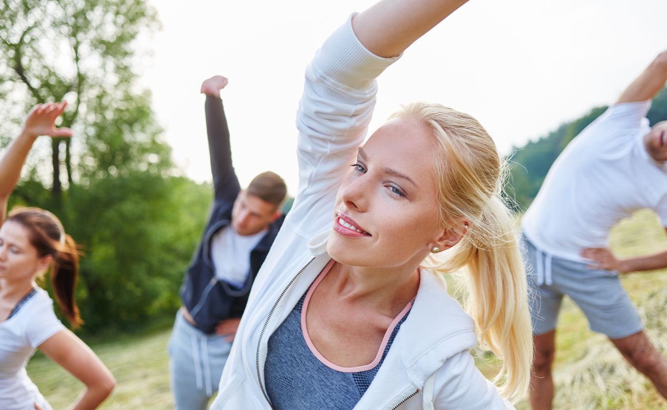 Photo of a group of young adult men and women outdoors engaged in group yoga.