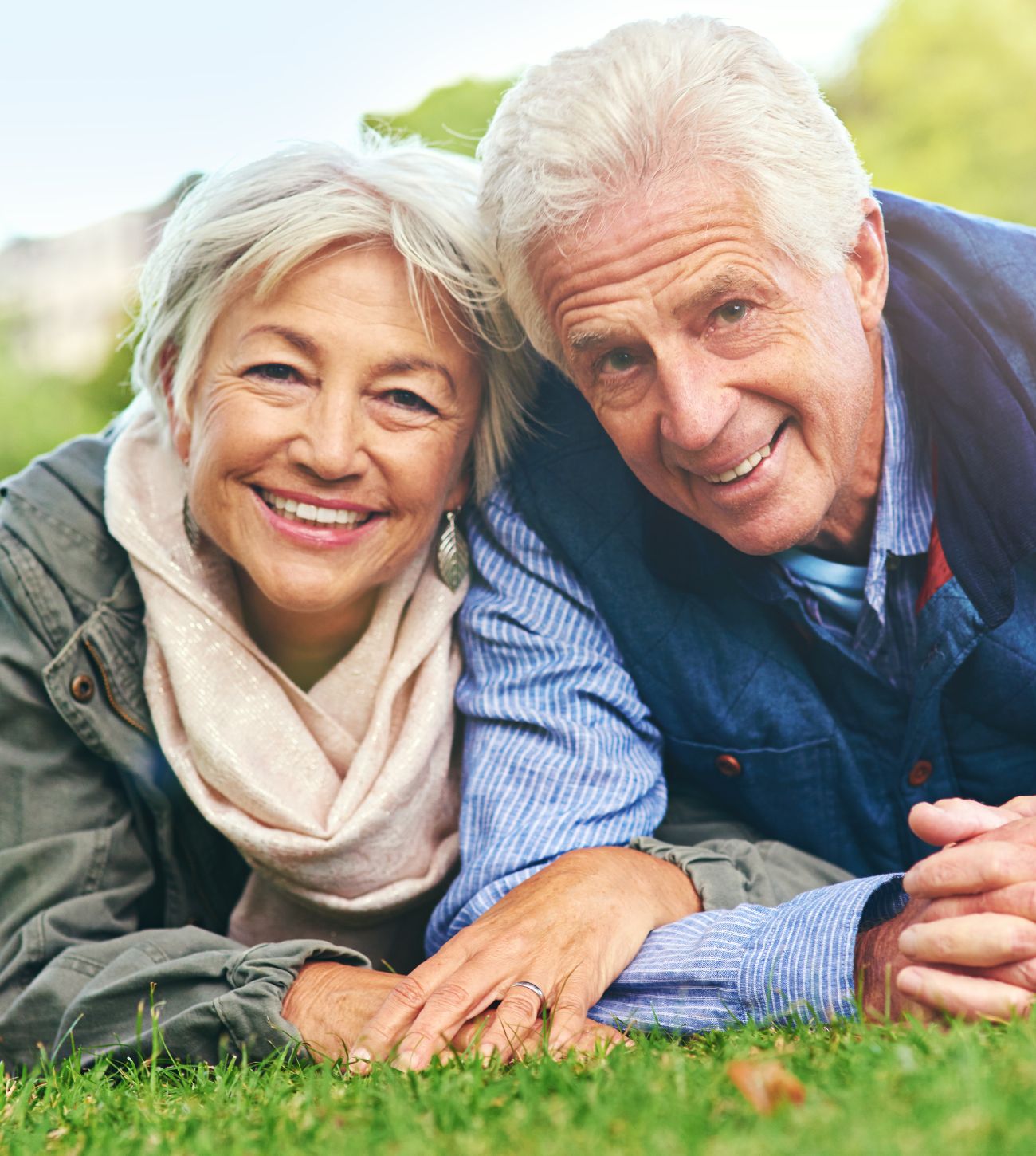 Photo of an older Caucasian couple snuggled together in the grass having their photo taken.