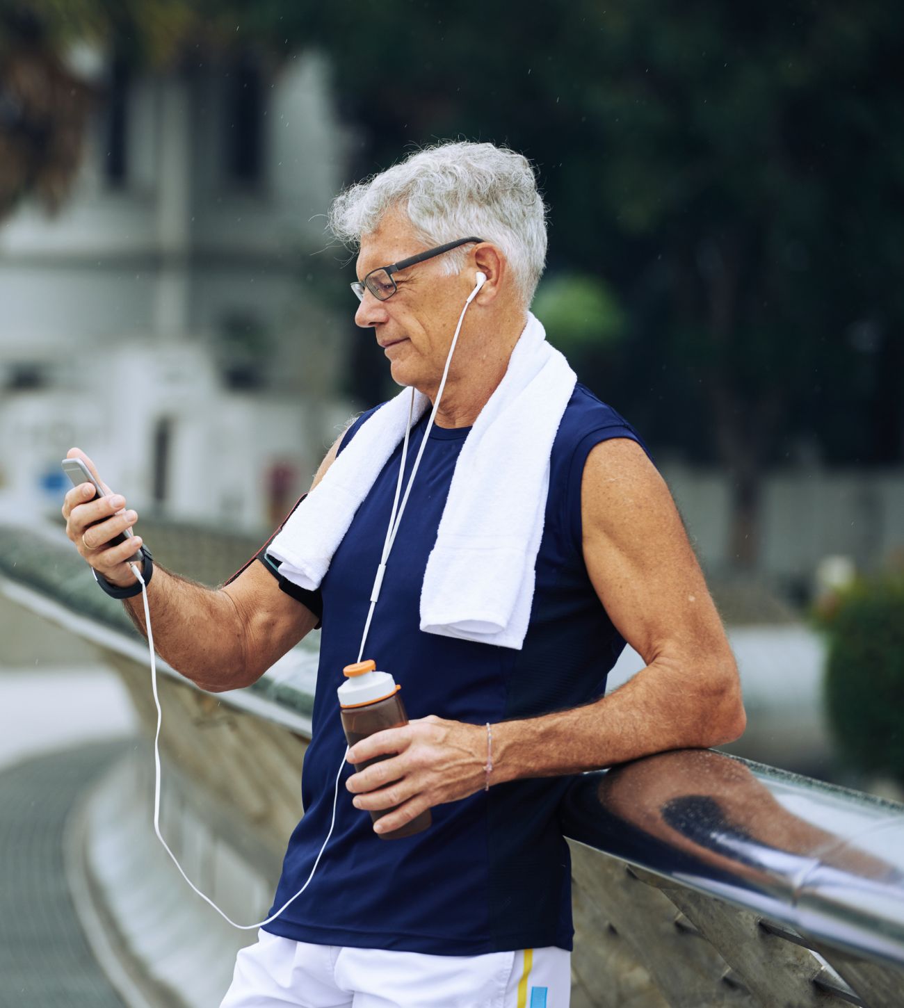 Photo of a mature adult man in his athletic gear pausing his exercise session to listen to something on his phone