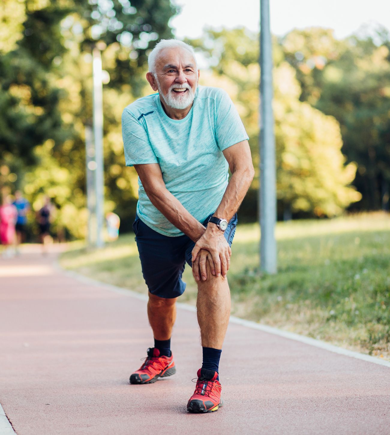 Photo of a mature man on an outdoor track stretching before he starts walking laps.