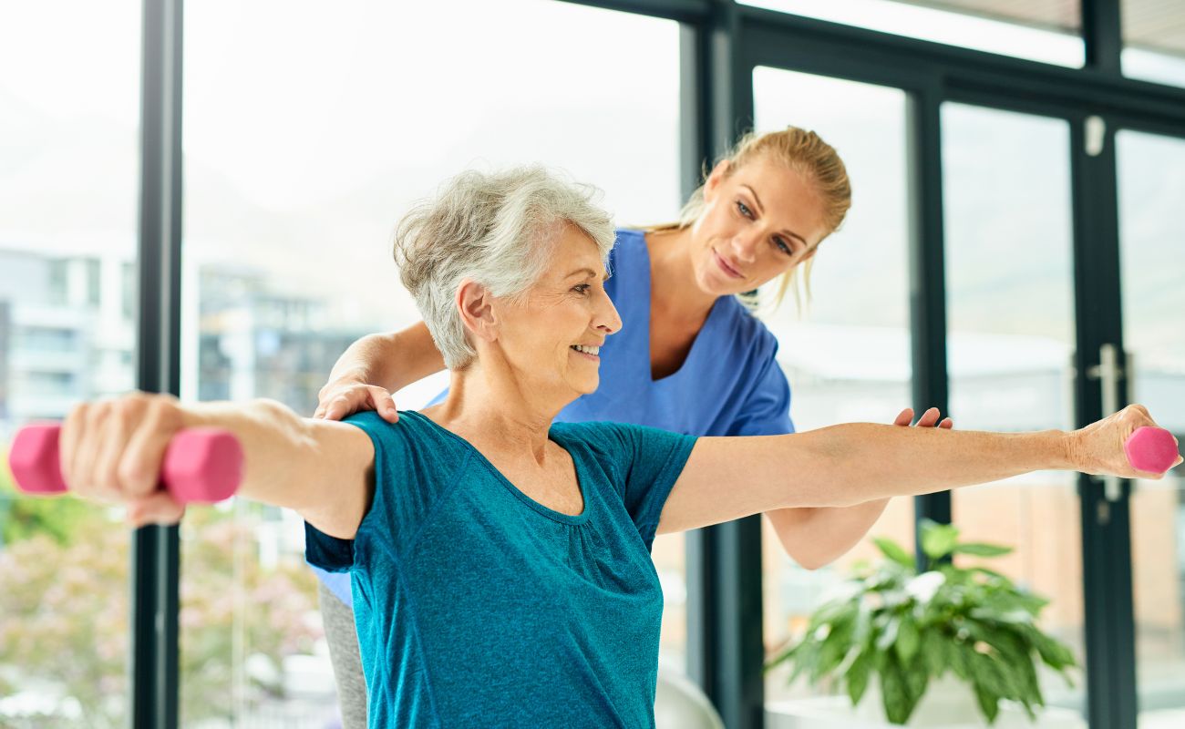 A personal trainer or physical therapist working indoors with a mature woman.