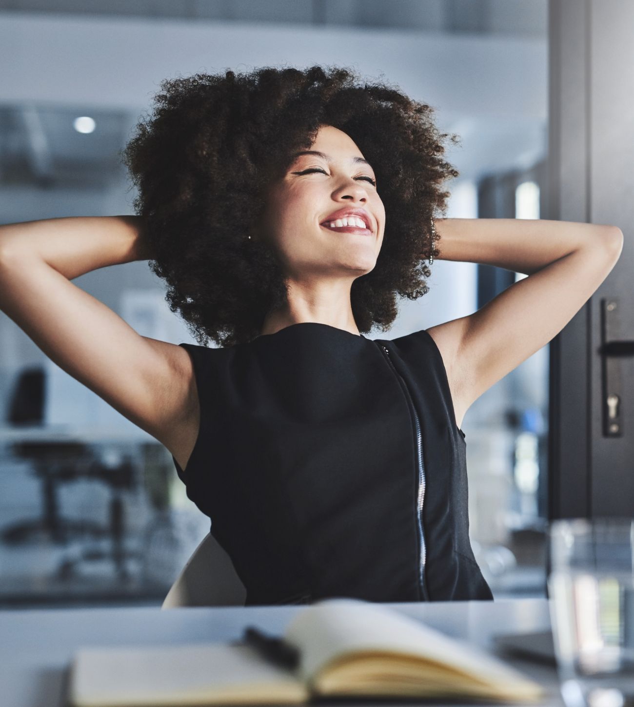 Photo of a young woman smiling and stretching at work.
