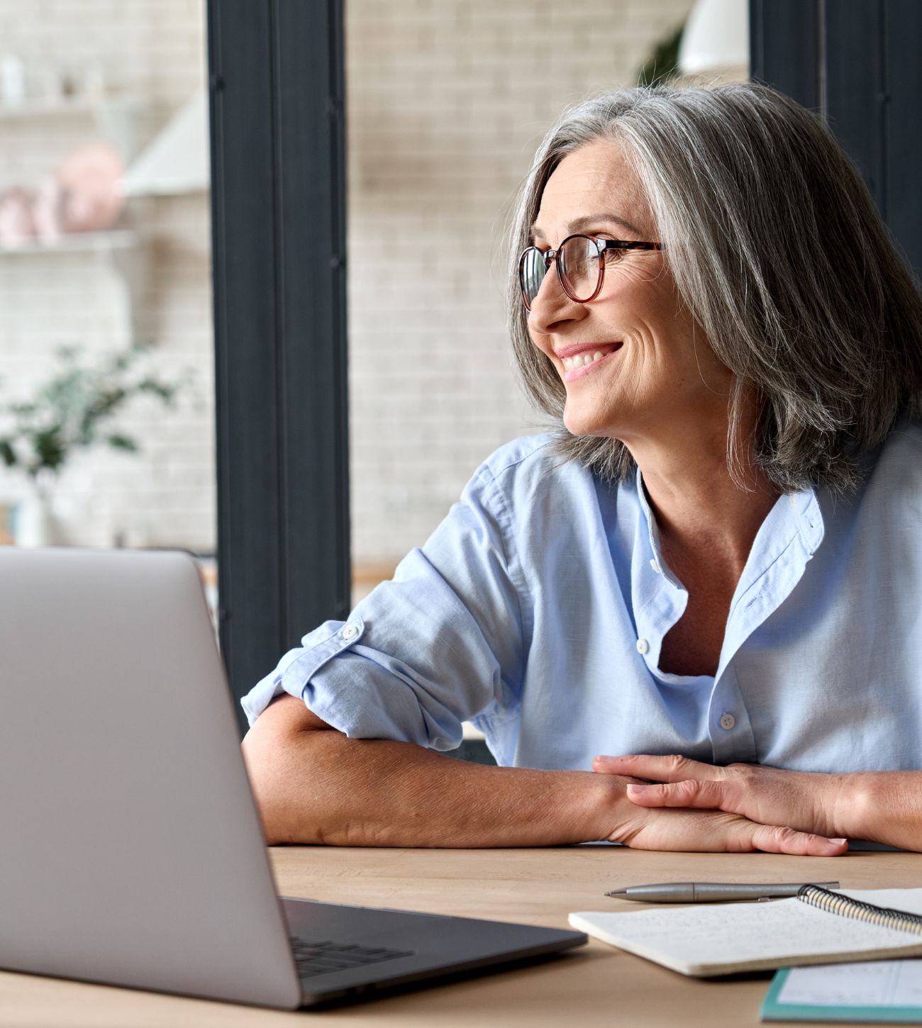 Photo of a mature woman sitting at her table with her computer in front of her.