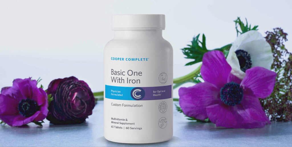 Bottle of Cooper Complete Basic One Daily With Iron Multivitamin and Mineral Supplement on a counter with flowers surrounding it