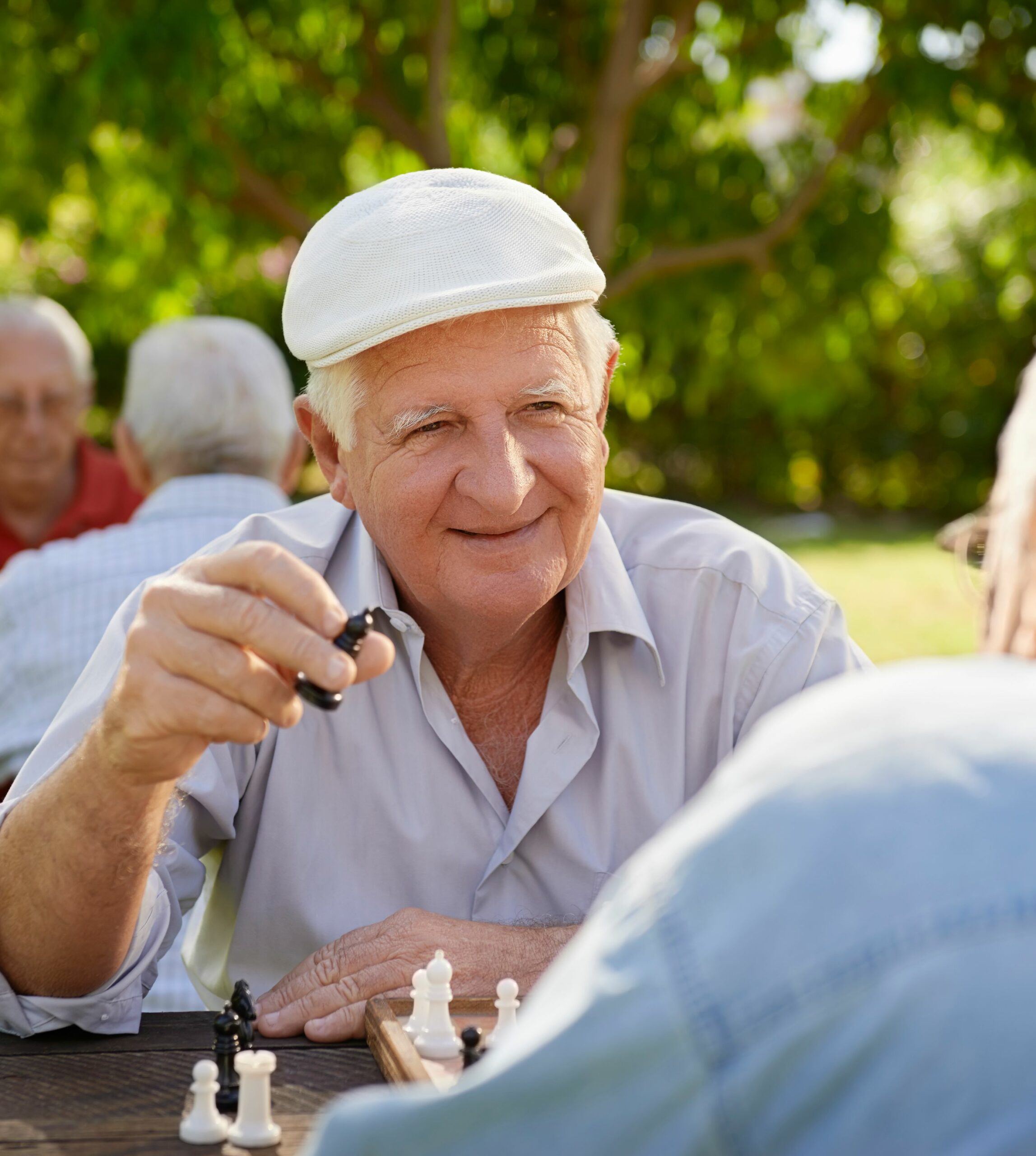 Image of several senior aged men happily playing chess outdoors.