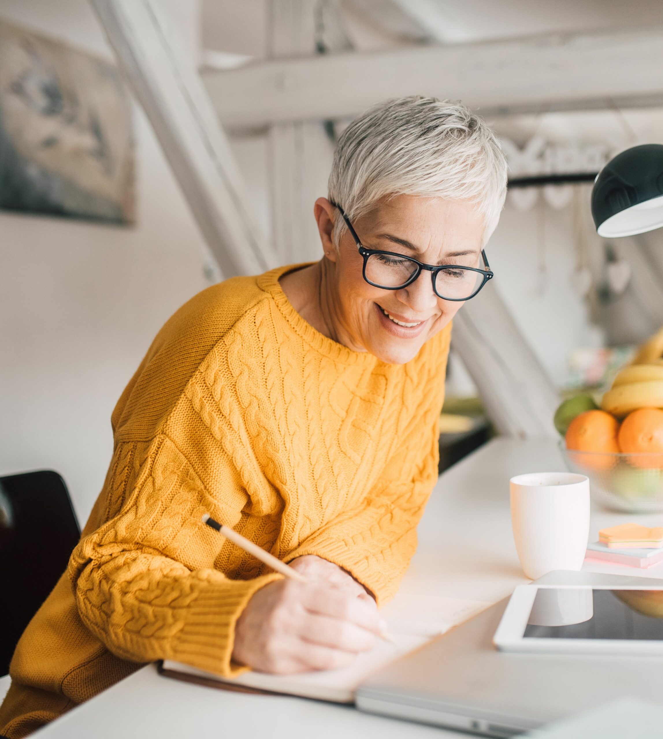 Photo of a mature woman journaling or making a list at the kitchen island.