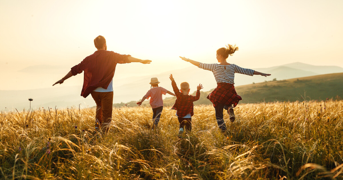 Photo of a couple with their two children cavorting in the grass and sunshine on an autumn day.