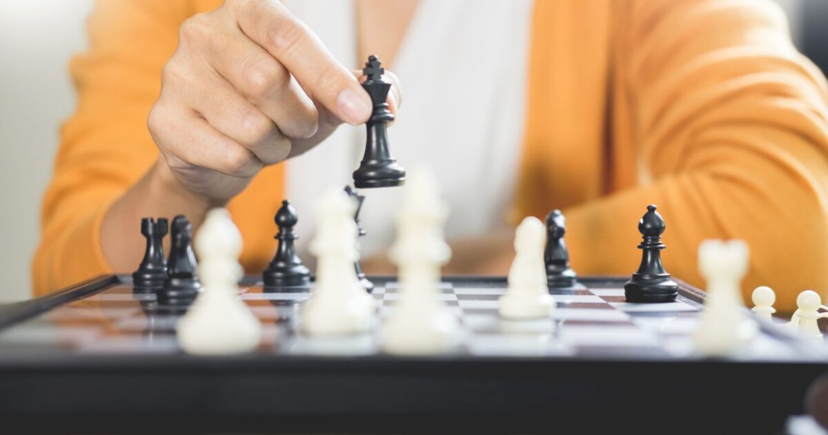 Image of a woman's hand moving a piece above a chessboard.