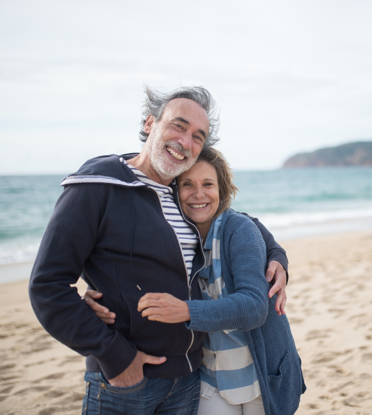 Older couple in their sweaters at the beach on a colder, blustery day.