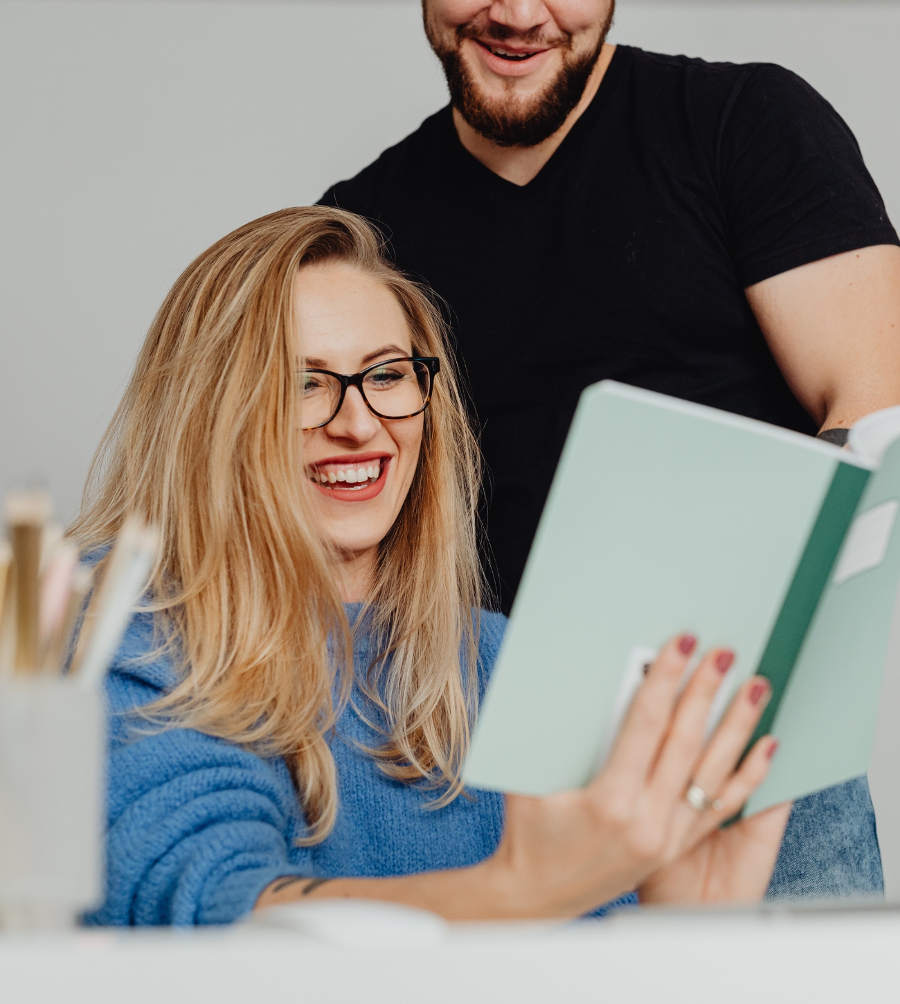 Couple laughing as the woman reads a journal and the man looks on.