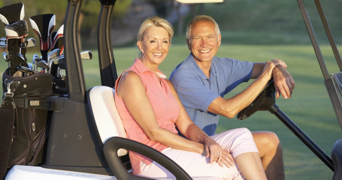 Photo of an adult couple 55+ in a golf cart on the golf course.