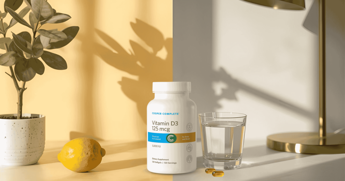Bottle of Cooper Complete Vitamin D3 125 mcg on a counter beside a lemon and a glass of water.