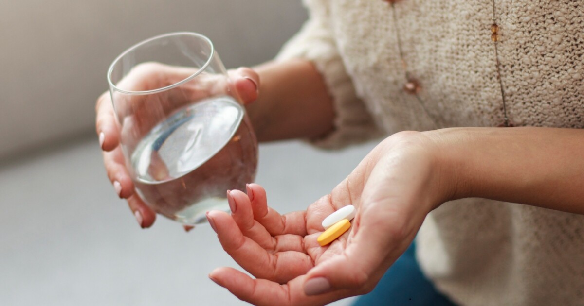 Photo of a woman holding a glass of water and two types of tablets.