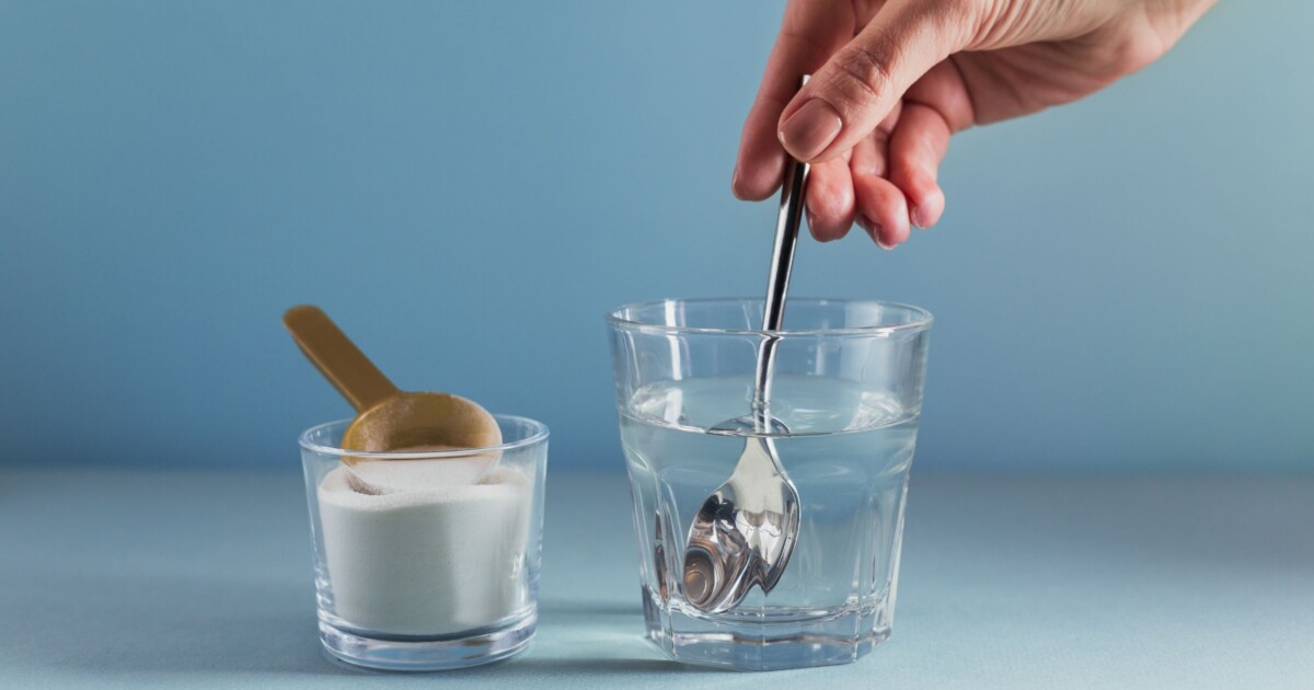 A feminine hand stirring white powder (creatine) into a clear glass of water.